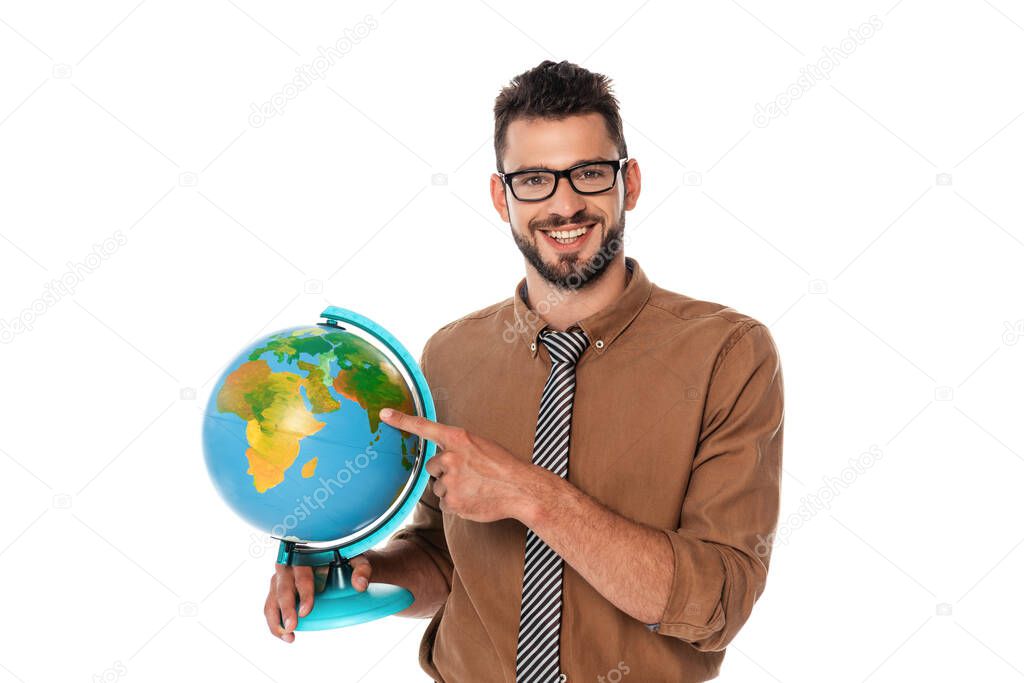 Bearded teacher smiling at camera while pointing with finger at globe isolated on white