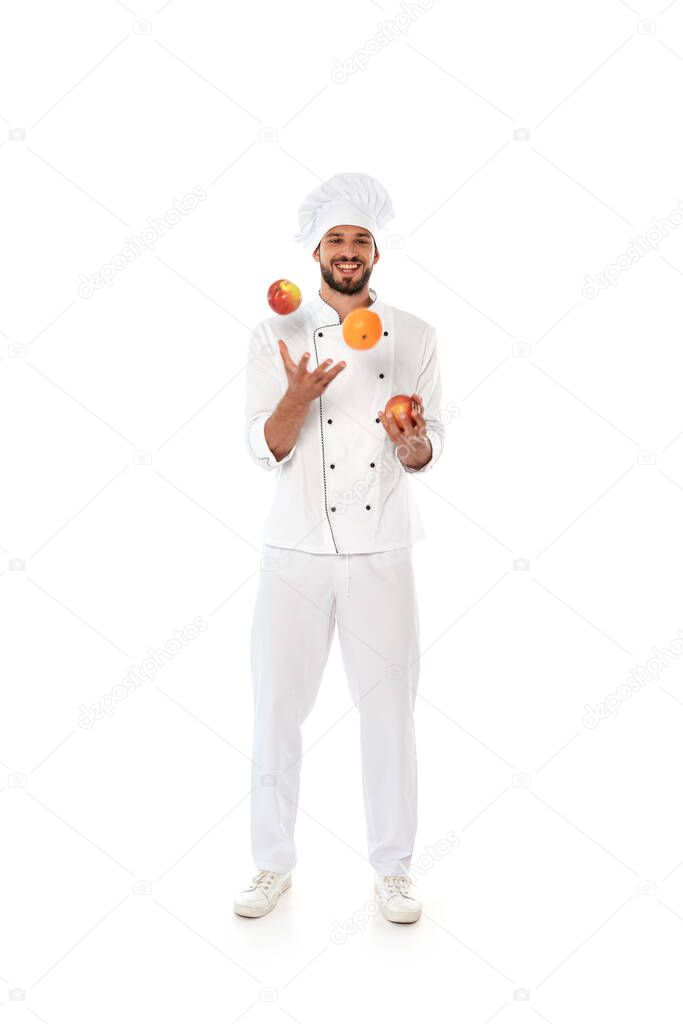 Smiling chef juggling fresh fruits on white background