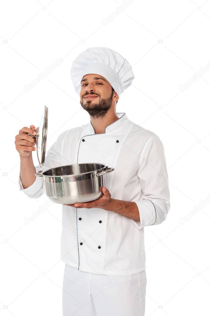 Handsome chef holding pan and cap while looking at camera isolated on white