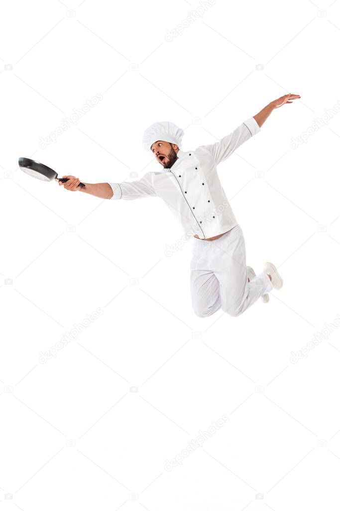 Excited chef holding frying pan while jumping isolated on white