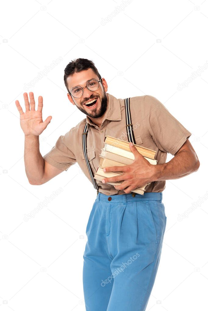 Positive nerd holding books and waving hand at camera isolated on white