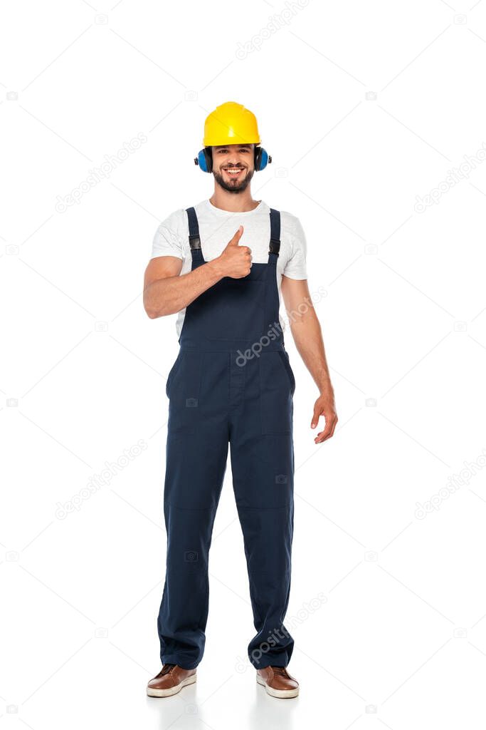 Handsome builder in workwear and hardhat smiling and showing thumb up gesture on white background
