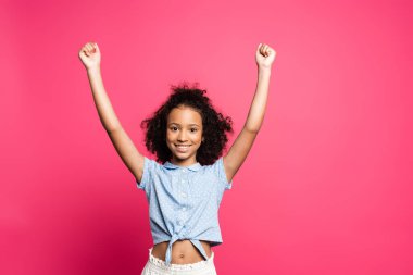 happy cute curly african american kid with hands in air isolated on pink clipart