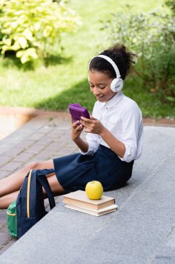 Sırt çantası, kitap ve öğle yemeği yanında kulaklıkla müzik dinleyen Afro-Amerikan okul kızı.