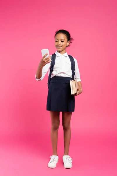 Glimlachend Afrikaans Amerikaans Schoolmeisje Met Boeken Smartphone Roze — Stockfoto