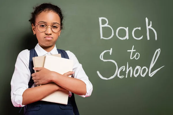 Upset African American Schoolgirl Books Back School Inscription Green Chalkboard — Stock Photo, Image