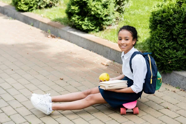 Gülümseyen Afro Amerikan Okul Kızı Kitaplar Elmalarla Panoda Oturuyor — Stok fotoğraf