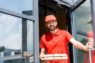 Gülümseyen garson, şehir caddesinde kafe yakınlarında pizza kutuları tutuyor. 