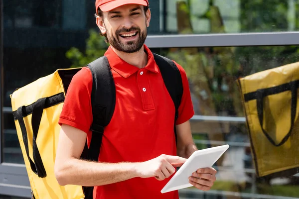 Mensajero Sonriente Con Mochila Térmica Mirando Cámara Mientras Usa Tableta — Foto de Stock