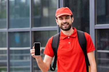 Şehir sokağında elinde boş ekranlı akıllı telefon tutan yakışıklı bir kurye. 