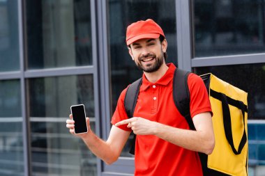 Gülümseyen teslimatçı, şehir caddesinde akıllı telefonu işaret ediyor. 