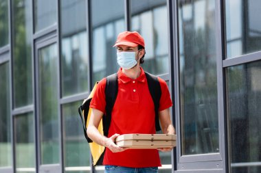 Tıbbi maskeli bir teslimatçı, elinde pizza kutuları var. 