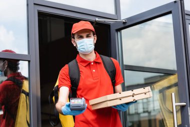 Pizza kutularını taşıyan kuryenin ve şehir sokağındaki ödeme terminalinin seçici odak noktası 