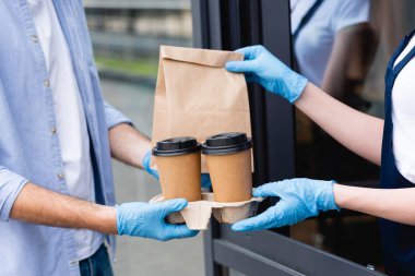 Kâğıt bardak ve garsondan kafe yakınlarında lateks eldivenli paket alan adam görüntüsü. 