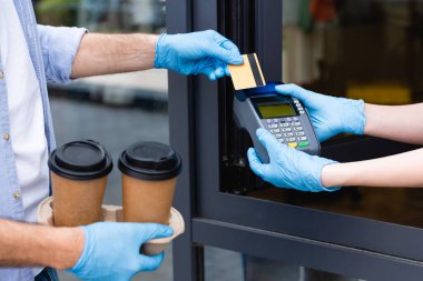 Kredi kartıyla ödeme yapan adam ve garsonun kafenin yanında ödeme terminali tutarken görüntüsü kesilmiş. 