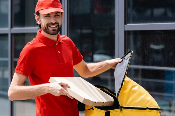 Correio Sorridente Olhando Para Câmera Enquanto Segurando Caixa Pizza Saco — Fotografia de Stock