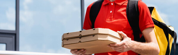 Panoramic crop of courier holding pizza boxes on urban street 