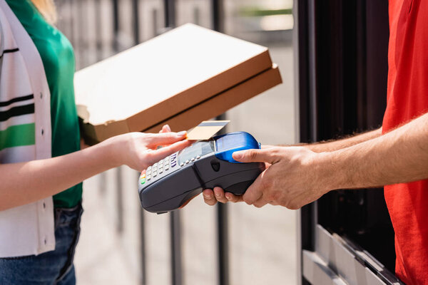 Cropped view of waiter holding payment terminal near woman with pizza boxes and credit card on urban street  