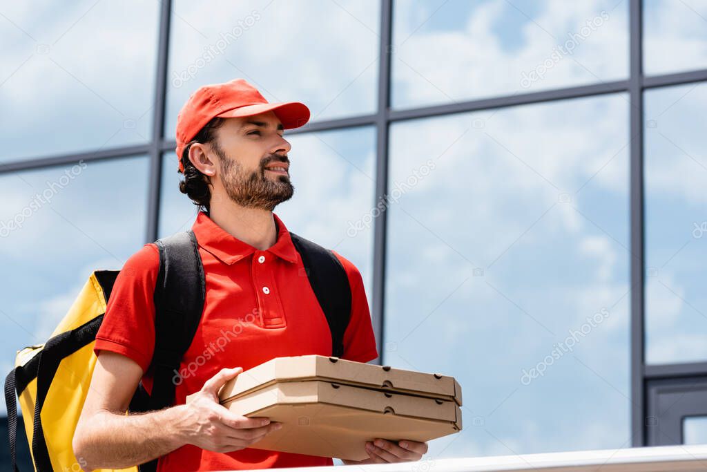 Handsome smiling courier in uniform holding pizza boxes on urban street 