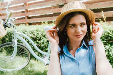 Bisiklet ve çitin yanında hasır şapkaya dokunan çekici bir kadın.