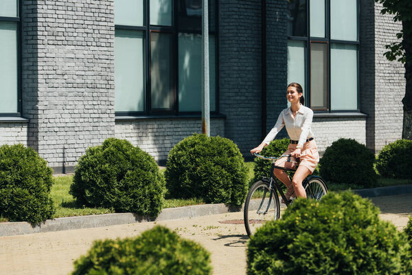 selective focus of happy businesswoman riding bicycle near modern building 