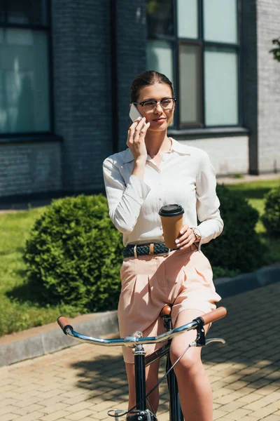 Attraktive Forretningskvinde Briller Taler Smartphone Holder Papir Kop Nær Cykel - Stock-foto