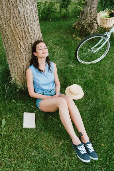 木の幹や自転車本やわらの帽子の近くに草の上に座って幸せな女性の高い角度のビュー — ストック写真