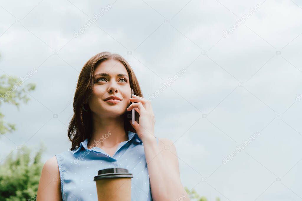 low angle view of businesswoman holding disposable cup and talking on smartphone against cloudy sky 
