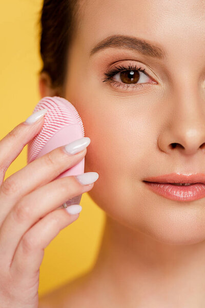 close up view of beautiful woman using facial cleansing brush isolated on yellow