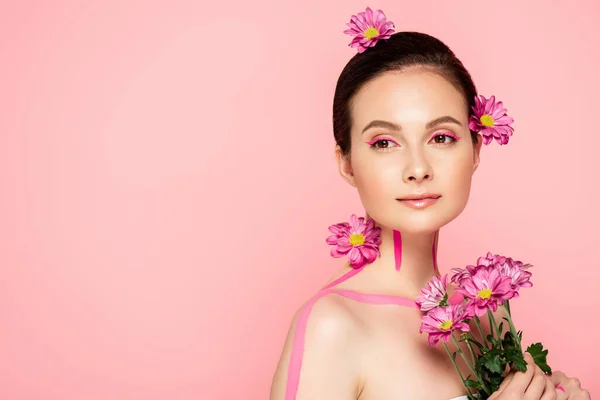 naked beautiful woman with pink lines on body and flowers in hair holding bouquet isolated on pink