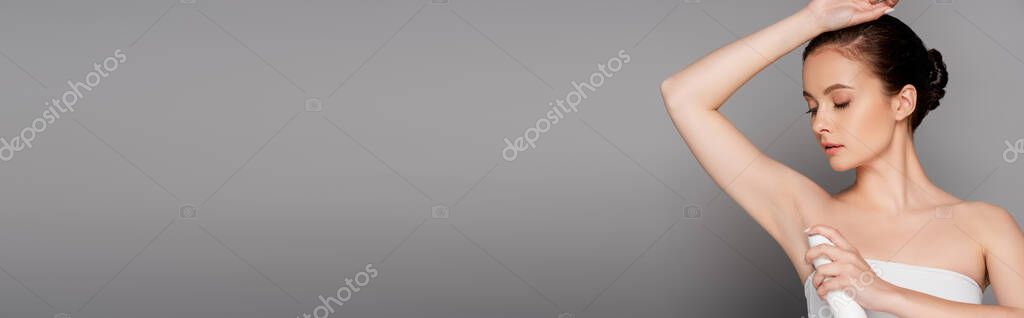 Beautiful brunette woman holding deodorant near armpit isolated on grey, panoramic shot