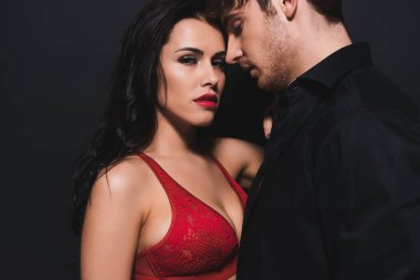 Yakışıklı bir erkek arkadaşın yanındaki kameraya bakan seksi genç kadın siyahta izole edilmiş. 