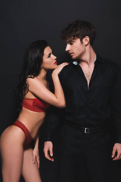 сексуальная молодая женщина в красном белье, смотрящая на красивого парня, изолированного от черного 