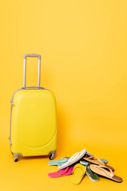 travel bag with colorful flip flops on yellow background clipart