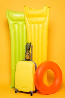 havuz kenarında ananas bulunan seyahat çantası sarı arka planda yüzer.