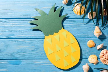 Deniz kabuklarına yakın kağıt ananas ve ahşap mavi arka planda palmiye yaprağı üst görünümü