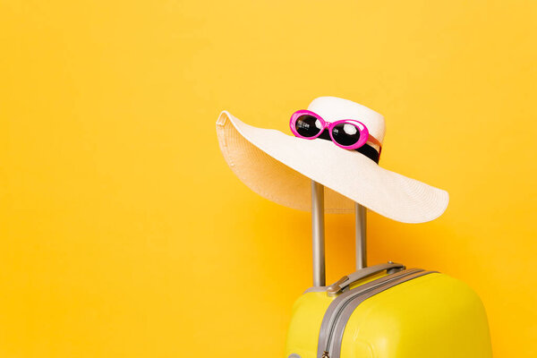 sun hat and sunglasses on suitcase handle on yellow background