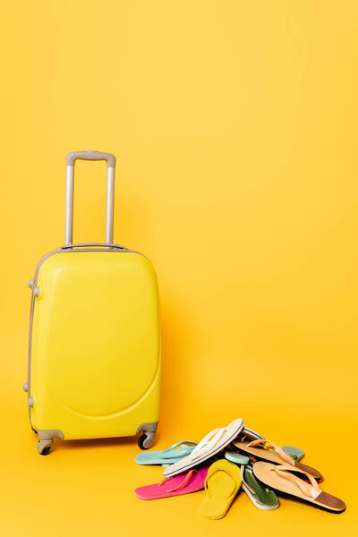 travel bag with colorful flip flops on yellow background