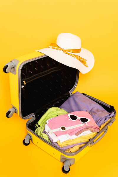 open travel bag with summer clothes and accessories on yellow background