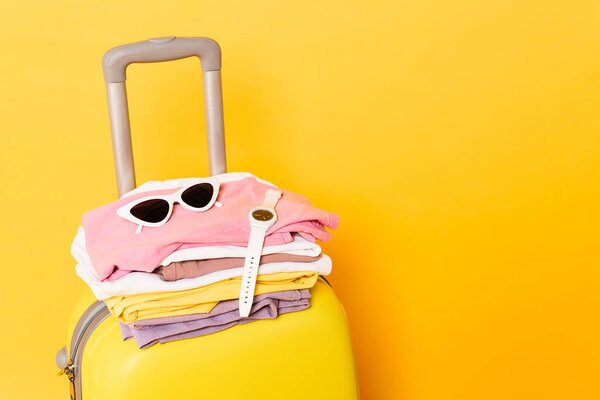 travel bag with summer clothes and accessories on yellow background