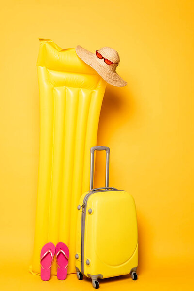 travel bag near pool float with beach accessories on yellow background