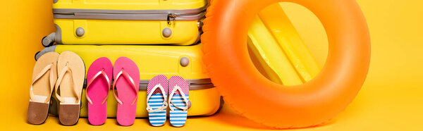 travel bags with family flip flops and pool floats on yellow, panoramic shot