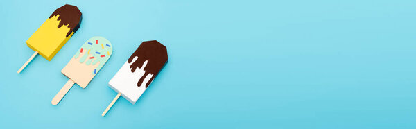 top view of paper ice cream with chocolate and sprinkles on blue background, panoramic shot