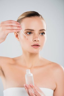 Gri üzerine izole edilmiş serumu uygularken elinde şişe ve pipet tutan çekici kadın. 