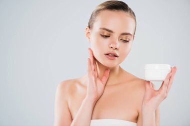 Gri üzerinde yüz kremi olan konteynıra bakan güzel bir kadın. 