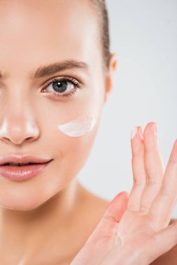 Gri üzerine izole edilmiş yüz kremi süren genç bir kadın manzarası. 