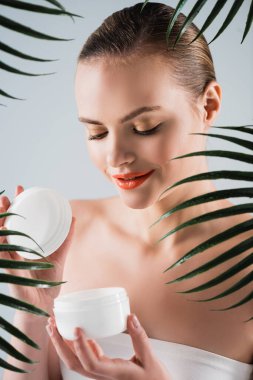 Makyajlı mutlu kız yüz kremi konteynırı ile beyaz palmiye yapraklarının yanında