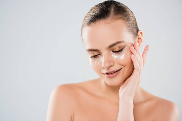 attractive and cheerful woman touching eye patch isolated on grey