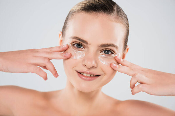 smiling and naked woman touching eye patches isolated on grey