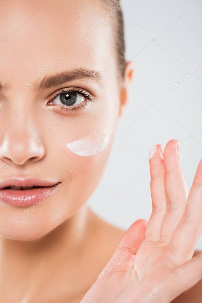 cropped view of young woman applying face cream isolated on grey 